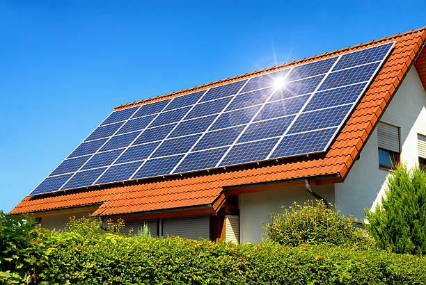 solar panel on a red roof reflecting the sun and the cloudless blue sky